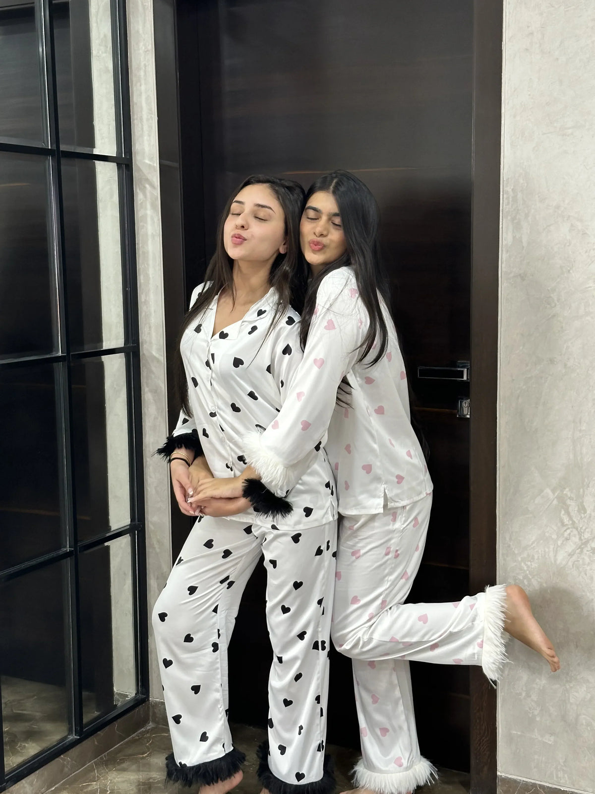 Two women in matching white heart print pajamas hugging in a cozy indoor setting
