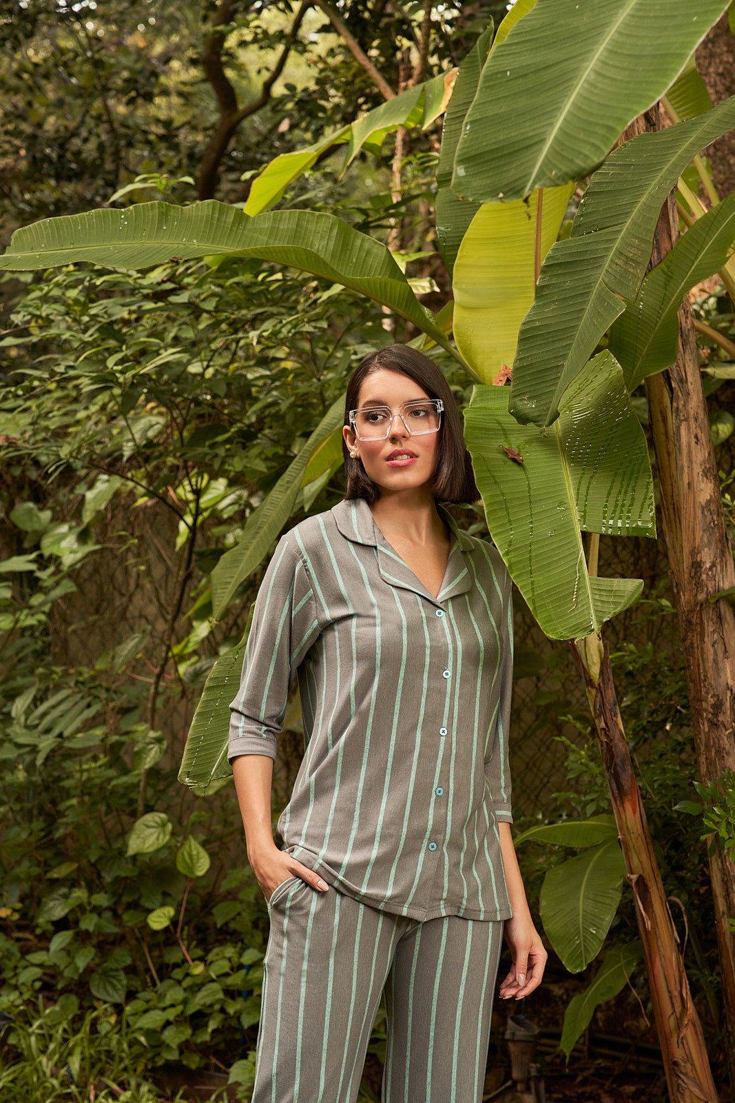 Woman wearing gray and light blue striped loungewear co-ord set standing outdoors by large green tropical leaves