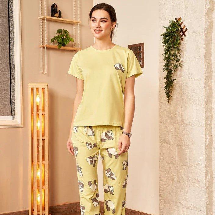 Woman wearing yellow panda print pajamas standing in cozy room with warm lighting and plants