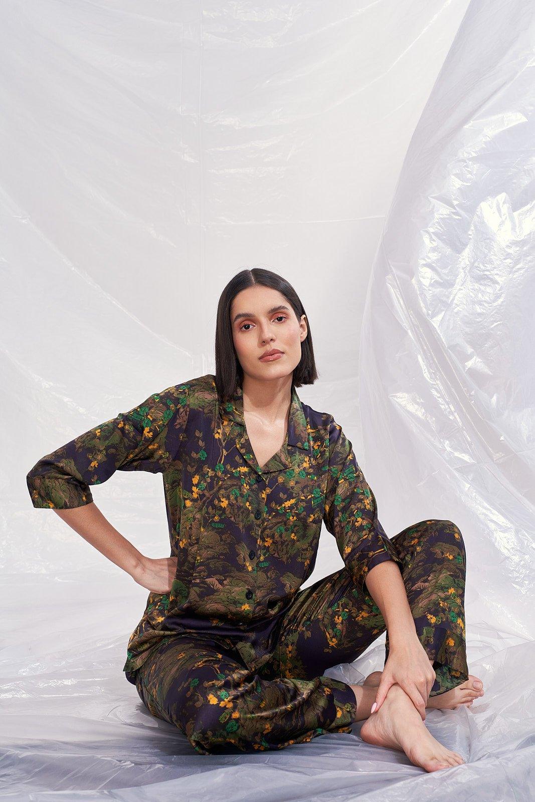 Woman sitting barefoot in dark floral satin velvet nightwear against white plastic backdrop