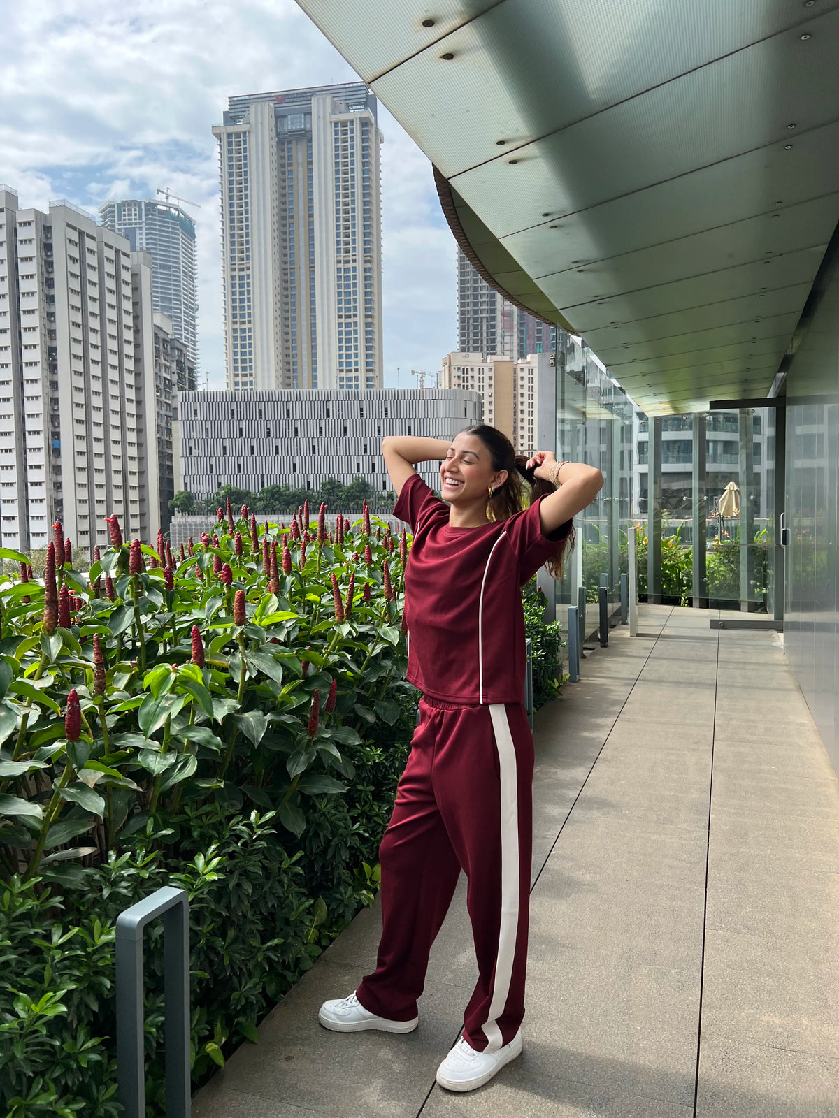 woman wearing Velure Maroon Serene Travel Set in a balcony with plants and buildings in the background