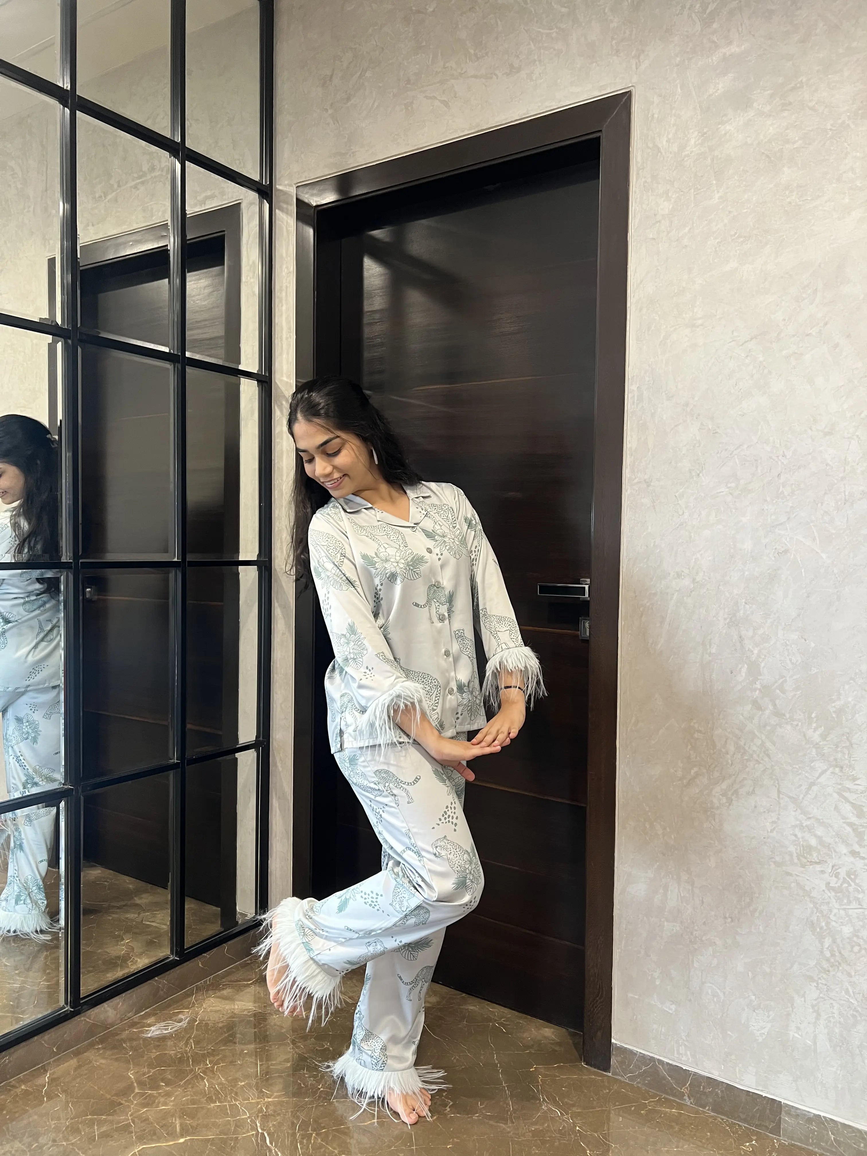 Woman in a satin nightwear standing in front of a mirror in a modern interior setting.