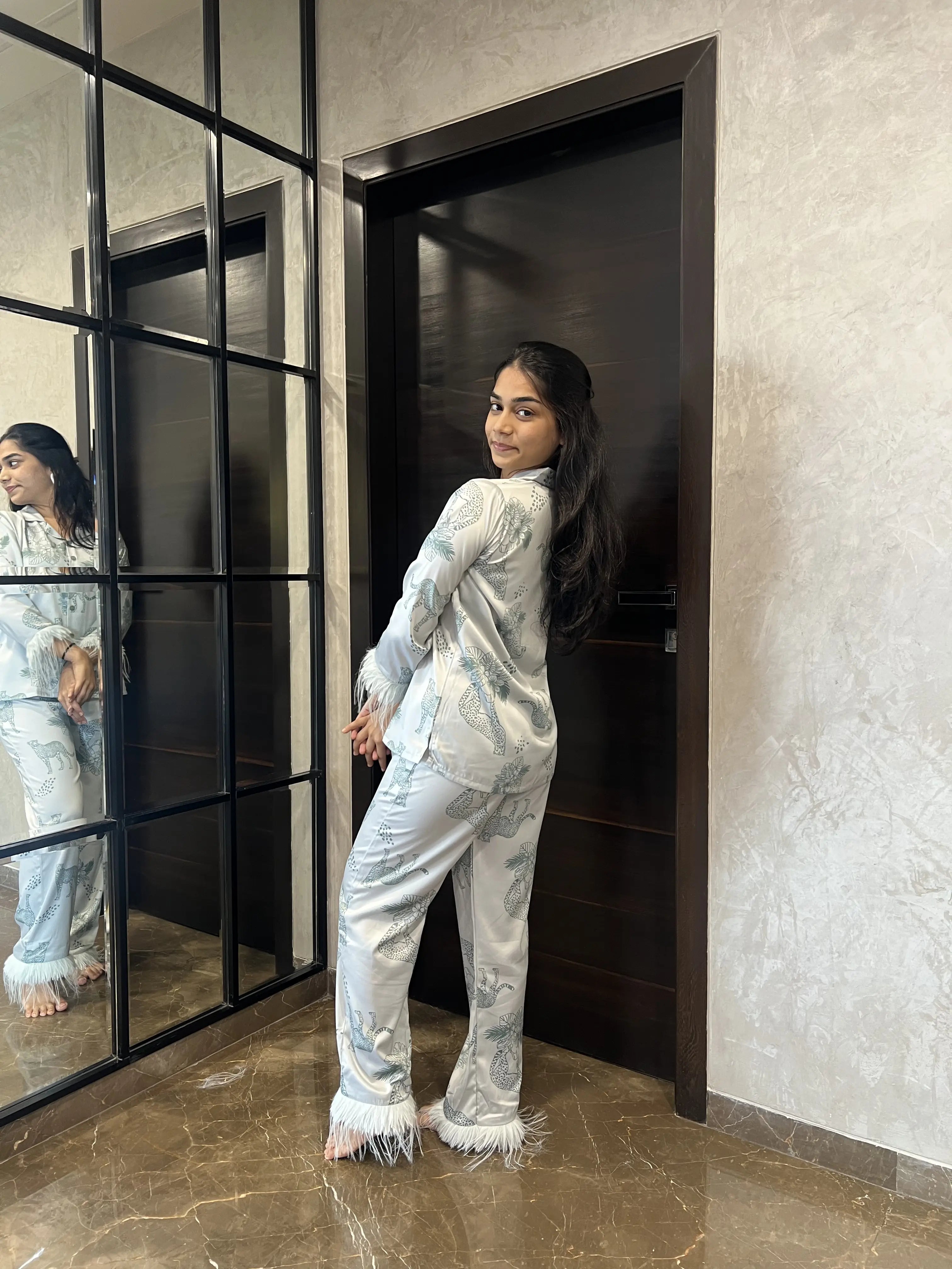 Woman in a satin nightwear standing in front of a mirror in a modern interior setting.