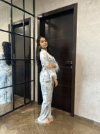 Woman in a satin nightwear standing in front of a mirror in a modern interior setting.