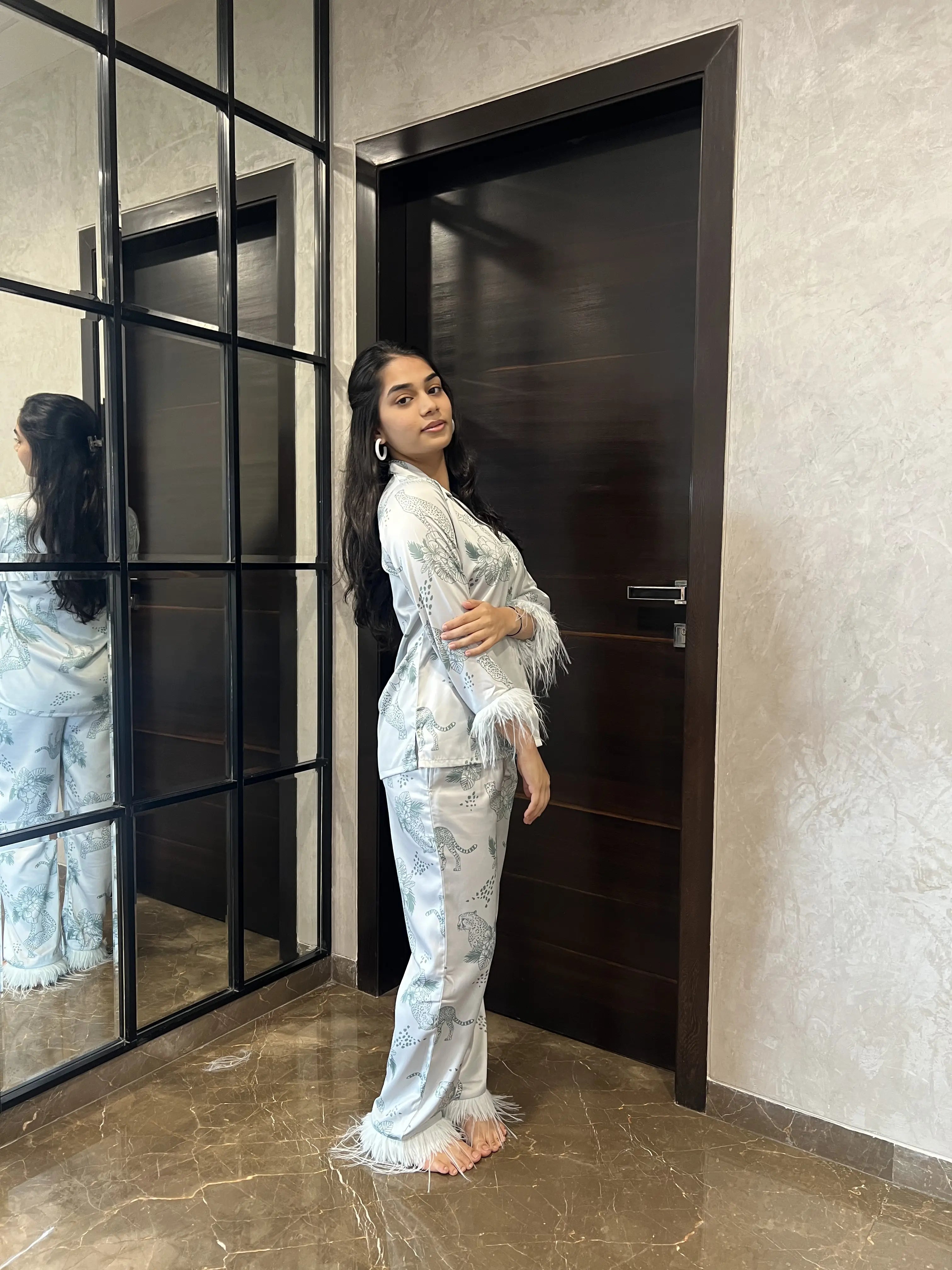Woman in a satin nightwear standing in front of a mirror in a modern interior setting.