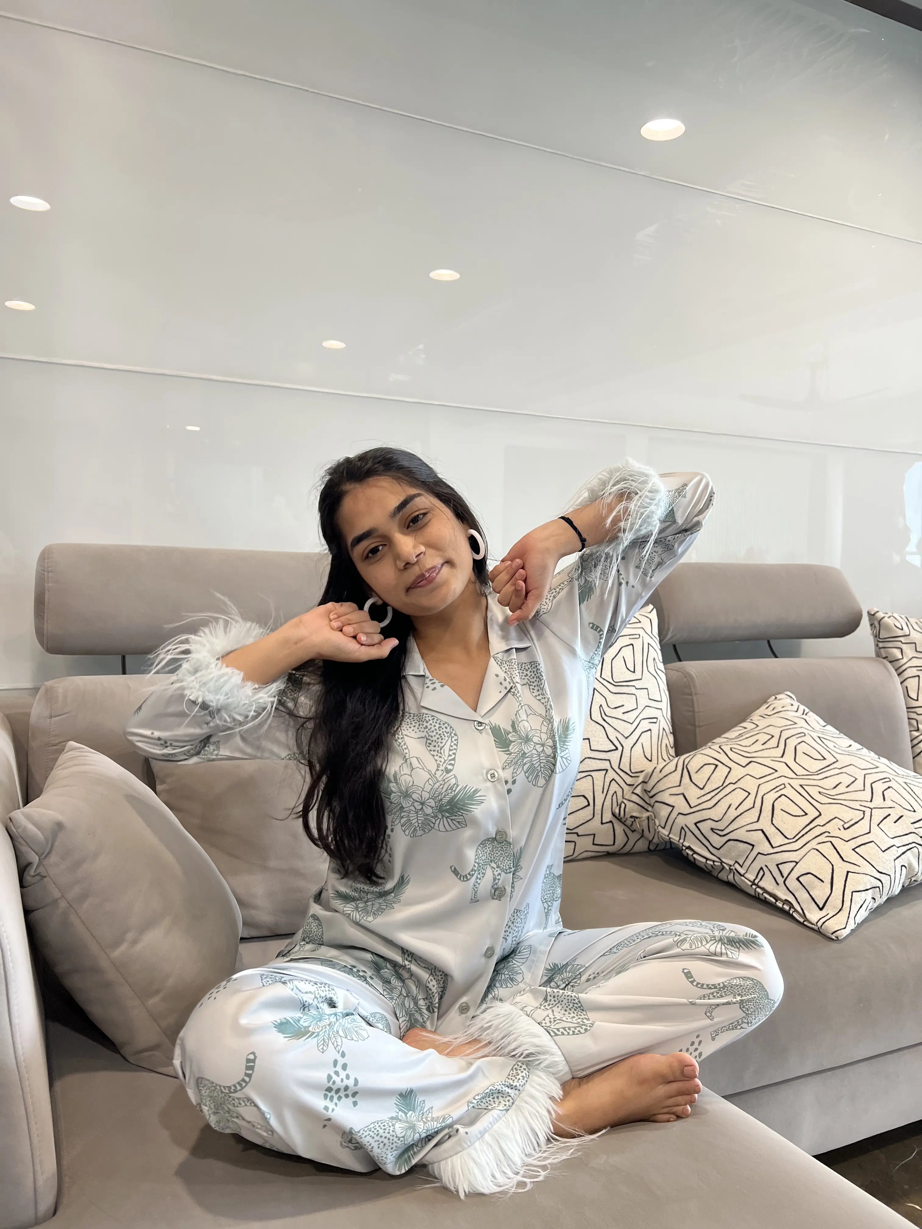 Woman in satin pajamas sitting on a couch in a modern living room.
