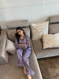 Woman in lavender pajamas sitting on a gray sofa with patterned cushions.