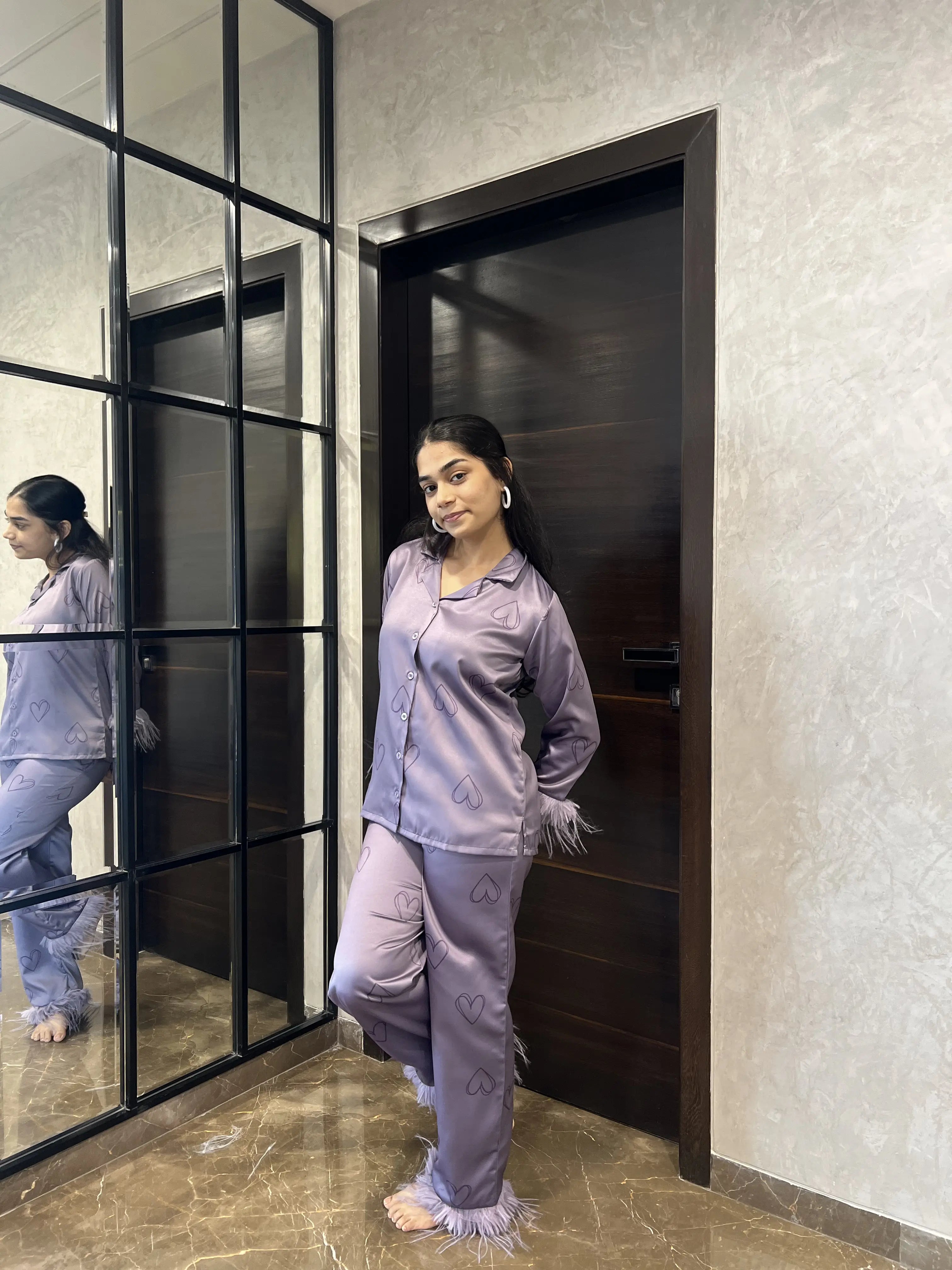 Woman in lavender pajama set standing in a room with a mirror and door.