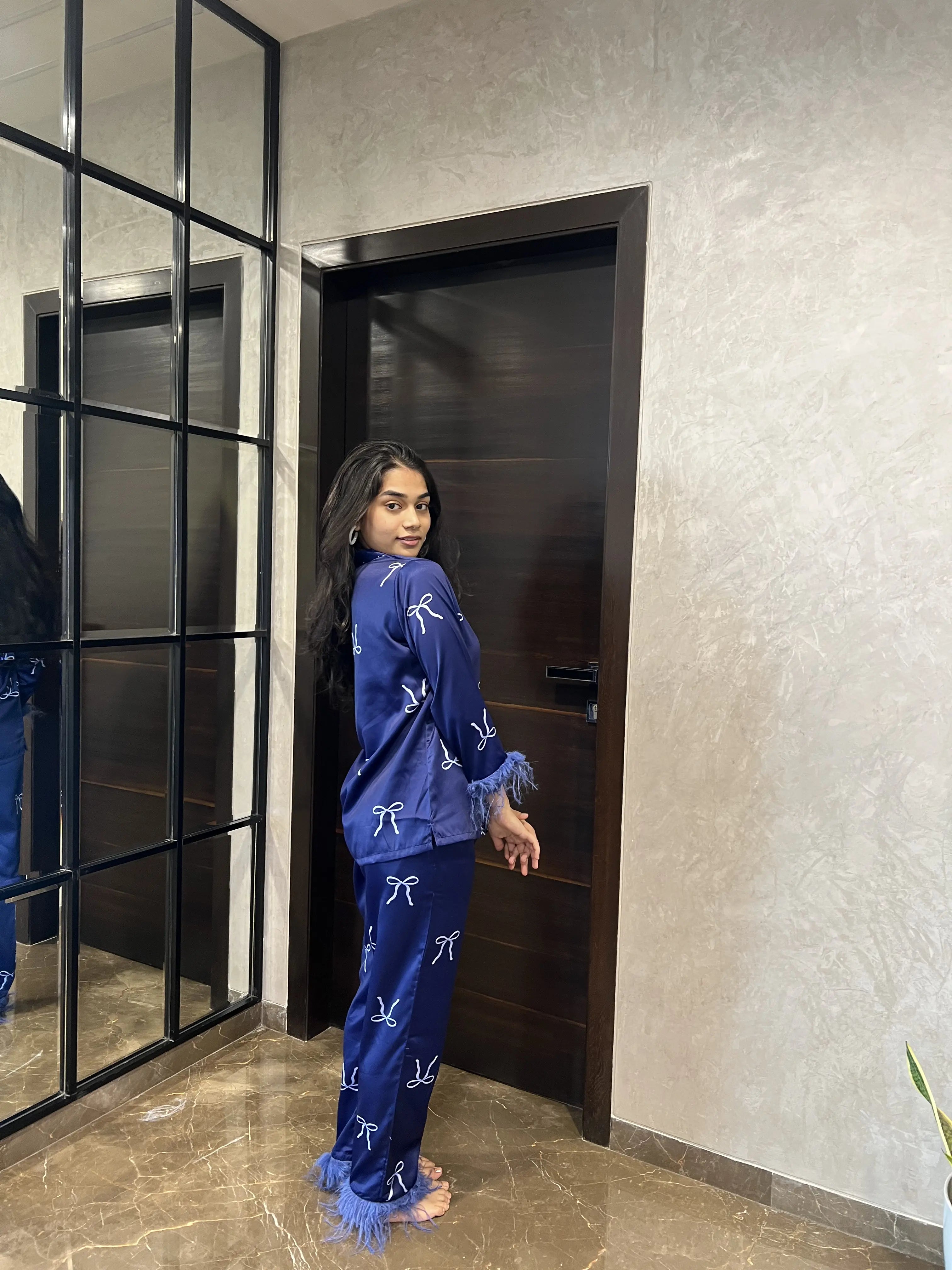 Woman in blue pajama set standing in a room with a mirror and door.
