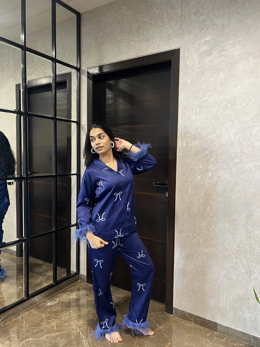 Woman in blue pajama set standing in a room with a mirror and door.