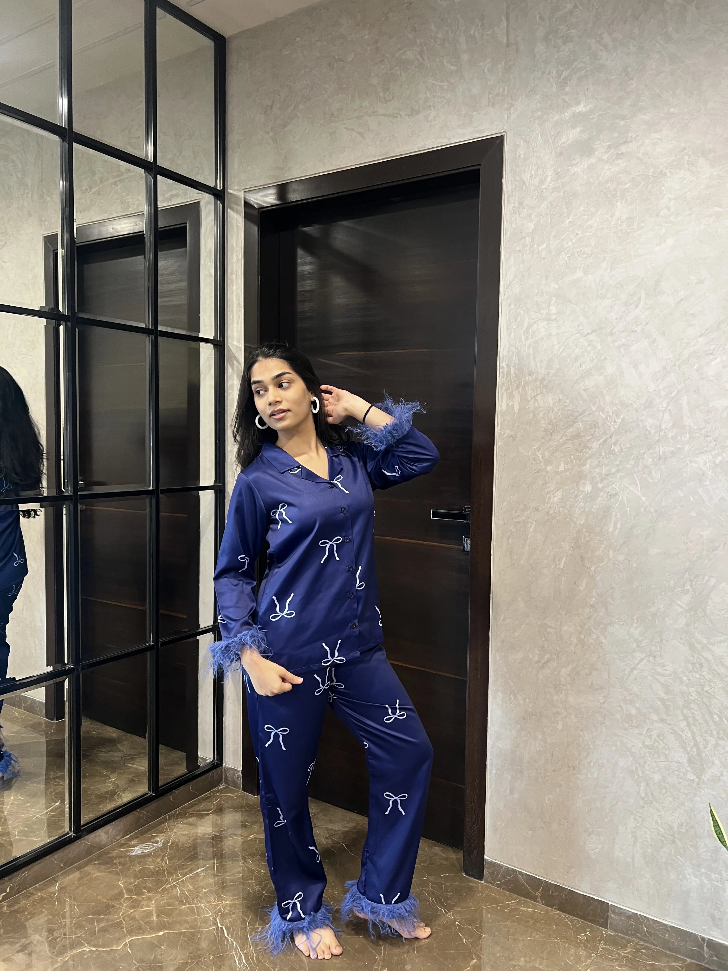 Woman in blue pajama set standing in a room with a mirror and door.