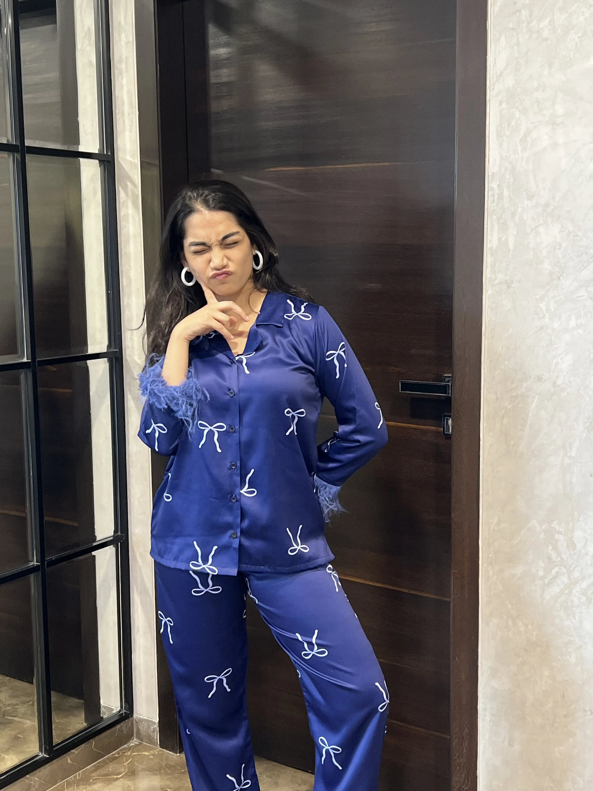 Woman wearing a blue pajama set with white patterns standing in front of a door.