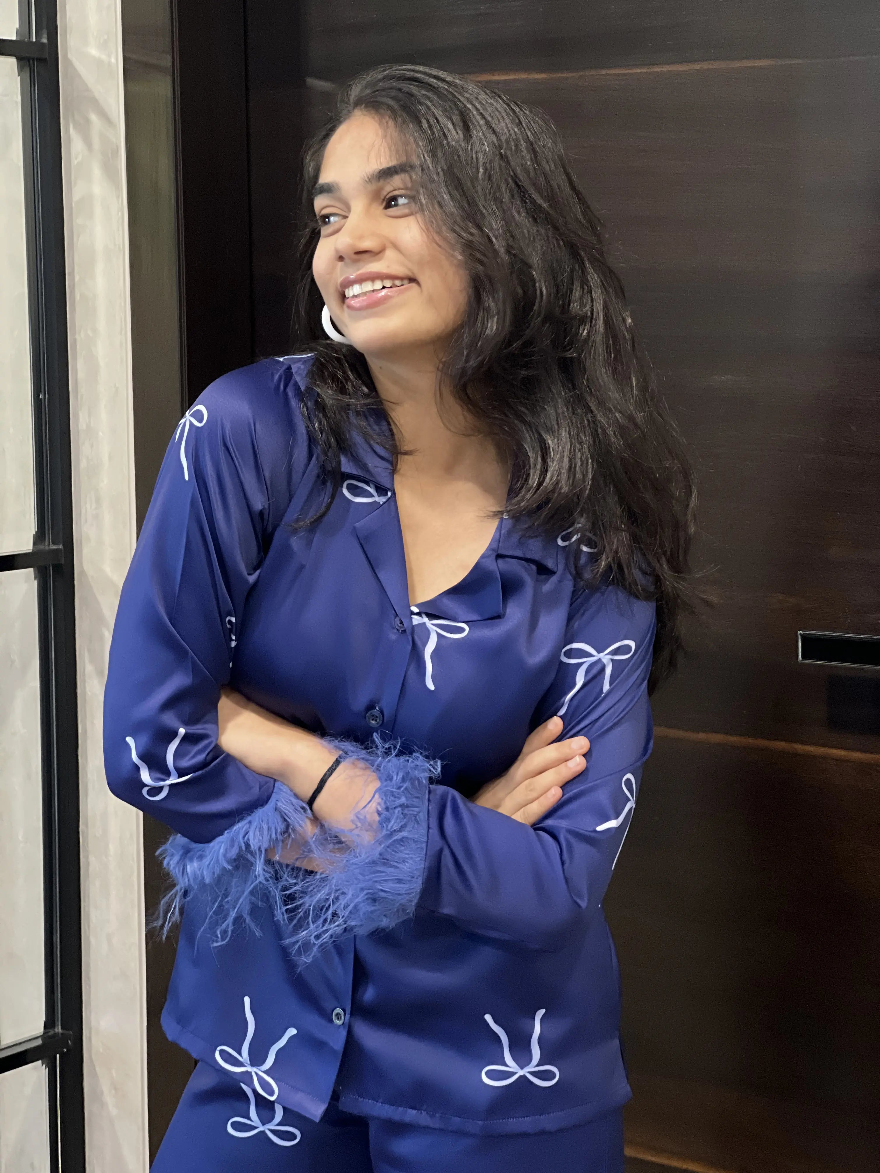 Woman wearing a blue outfit with white bows standing indoors.