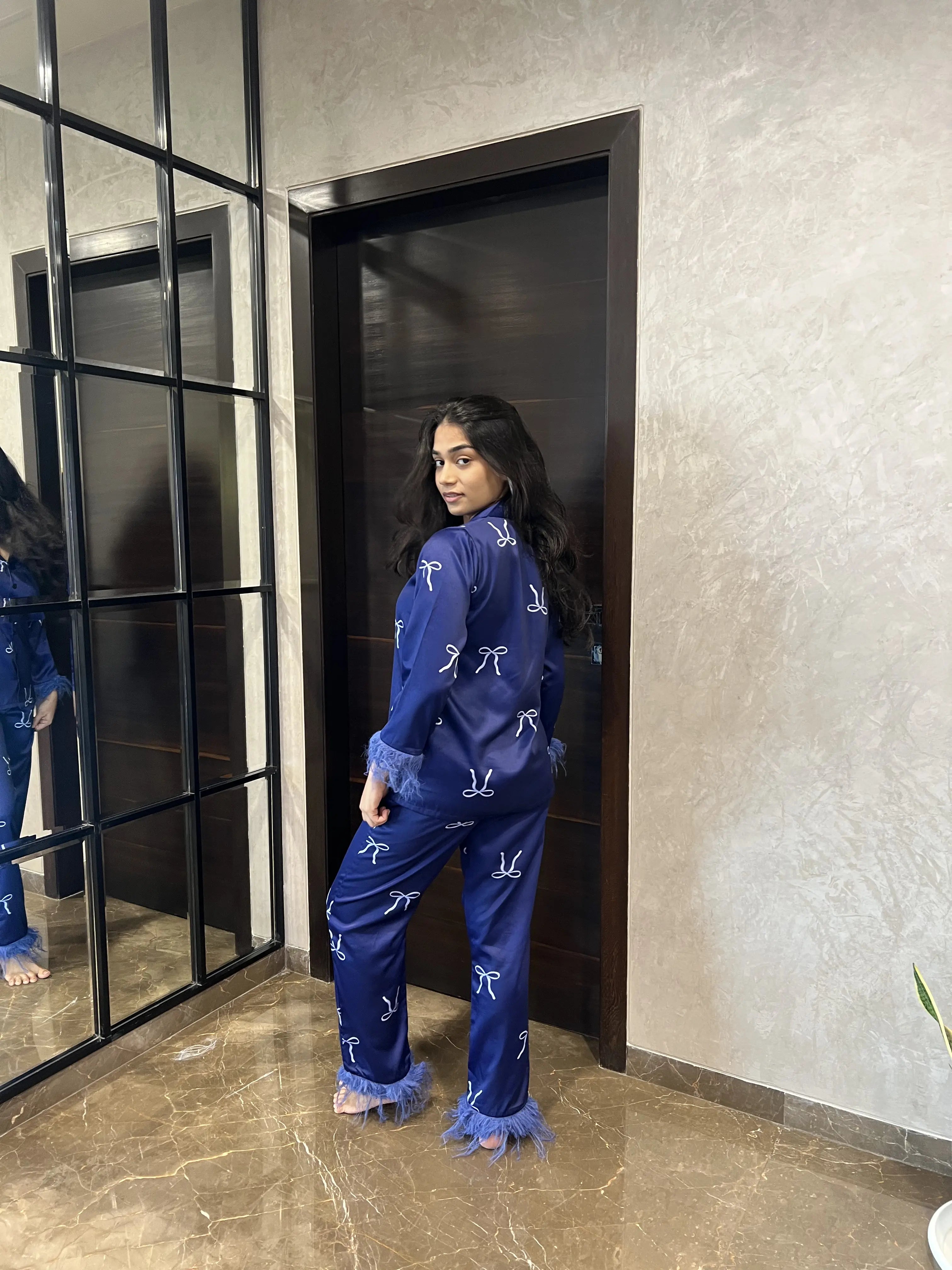 Person wearing a blue satin night suit with white bows standing in front of a mirror.